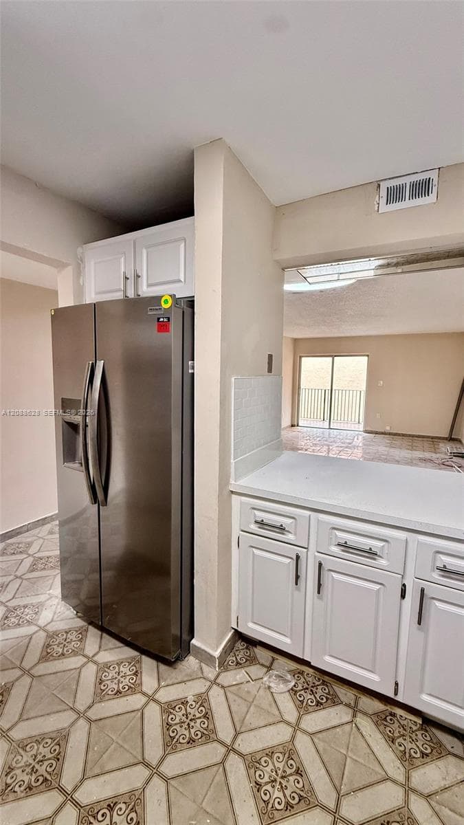 Kitchen area featuring stainless steel side-by-side refrigerator, white cabinetry, solid-surface countertops, and geometric-patterned tile flooring