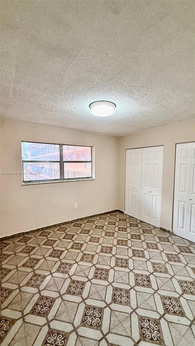 Room featuring patterned tile flooring, dual-panel closet doors, single-panel door, and a flush-mount light fixture