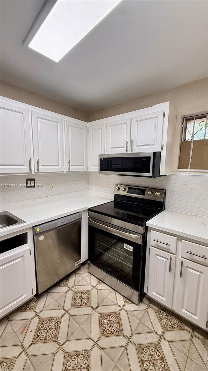 Kitchen featuring white shaker-style cabinetry, solid-surface countertops, subway tile backsplash, stainless steel dishwasher, and matching over-the-range microwave