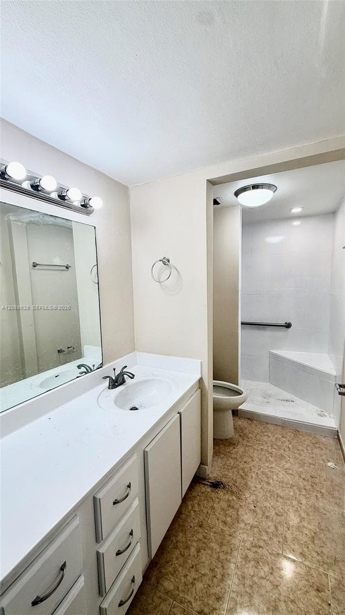 Bathroom featuring a vanity with white countertop, integrated sink, and four-light wall-mounted fixture, complete with a walk-in shower containing a built-in bench seat and grab bar