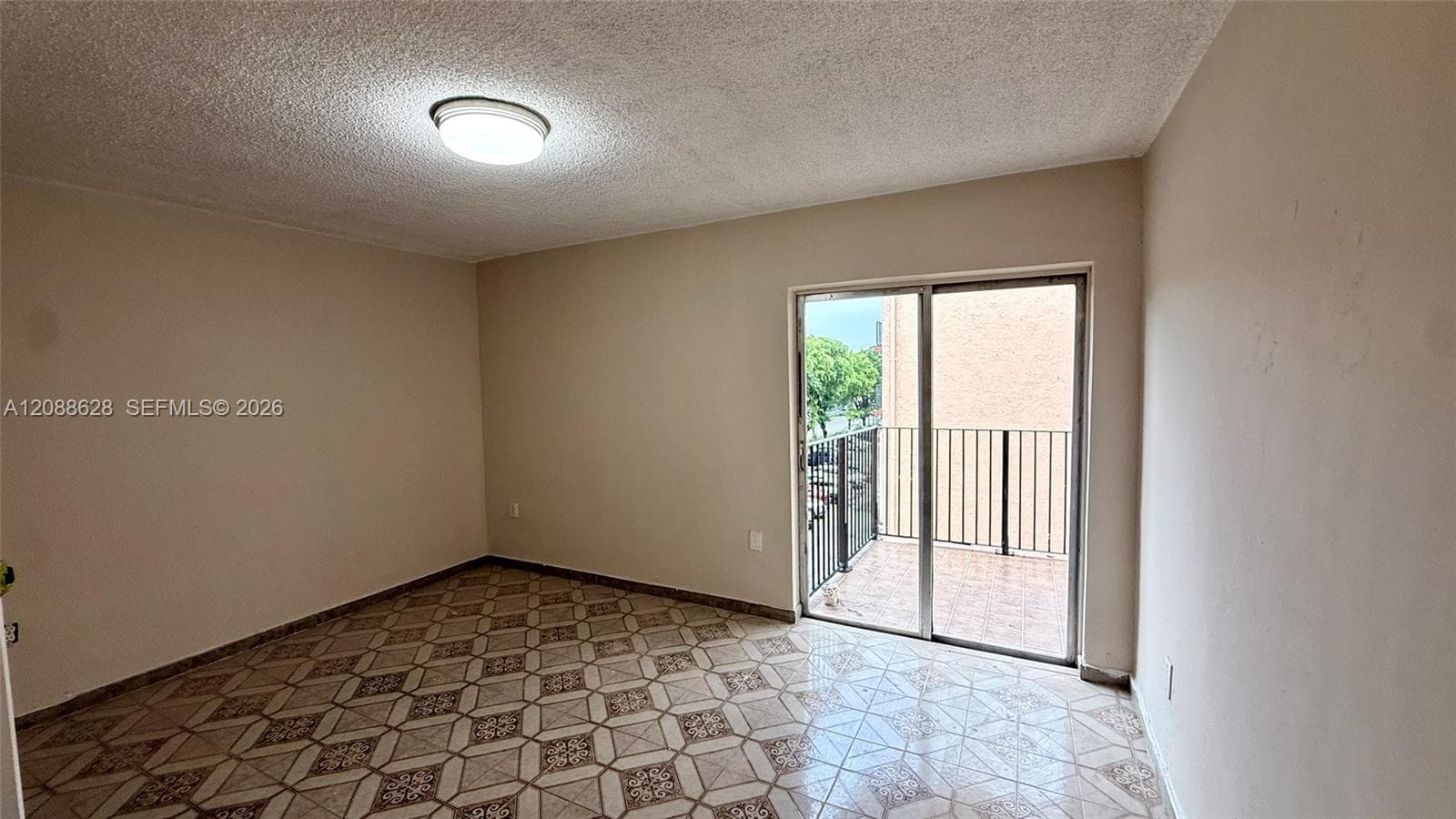 Interior room featuring decorative patterned tile flooring, sliding glass door, metal balcony railing, and flush-mount ceiling lighting