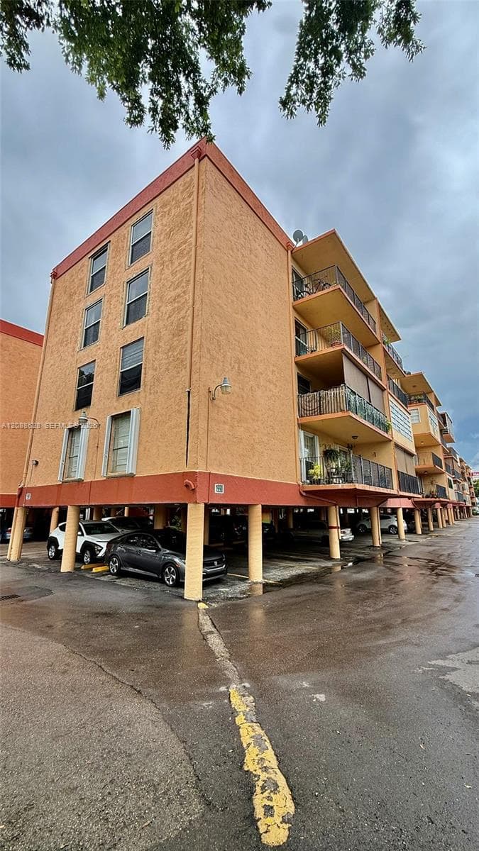 Multi-story building with textured stucco exterior, stacked cantilevered balconies, and ground-level covered parking