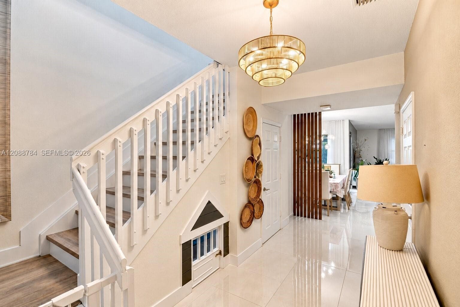 Wood-finish staircase with white balusters, polished tile flooring, and a tiered chandelier