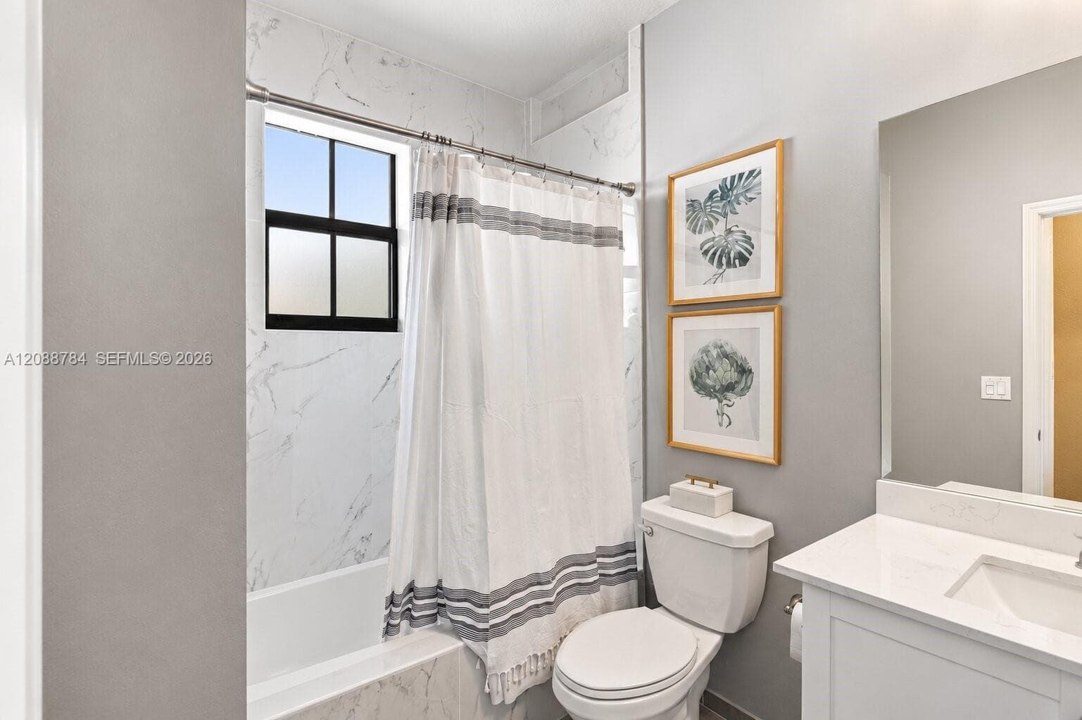 Tub/shower combination with tile surround, single vanity with integrated sink, large wall-mounted mirror, and black-framed window