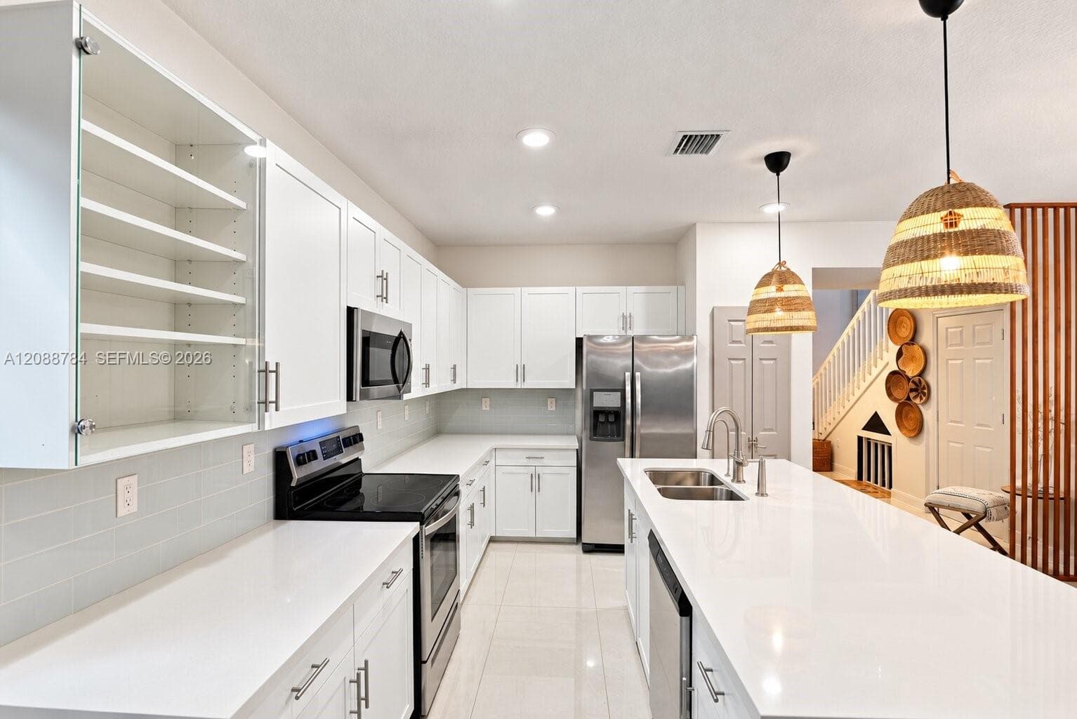 Kitchen featuring white cabinetry, solid-surface countertops, stainless steel appliances, a central island with dual-basin sink, and decorative woven pendant lighting