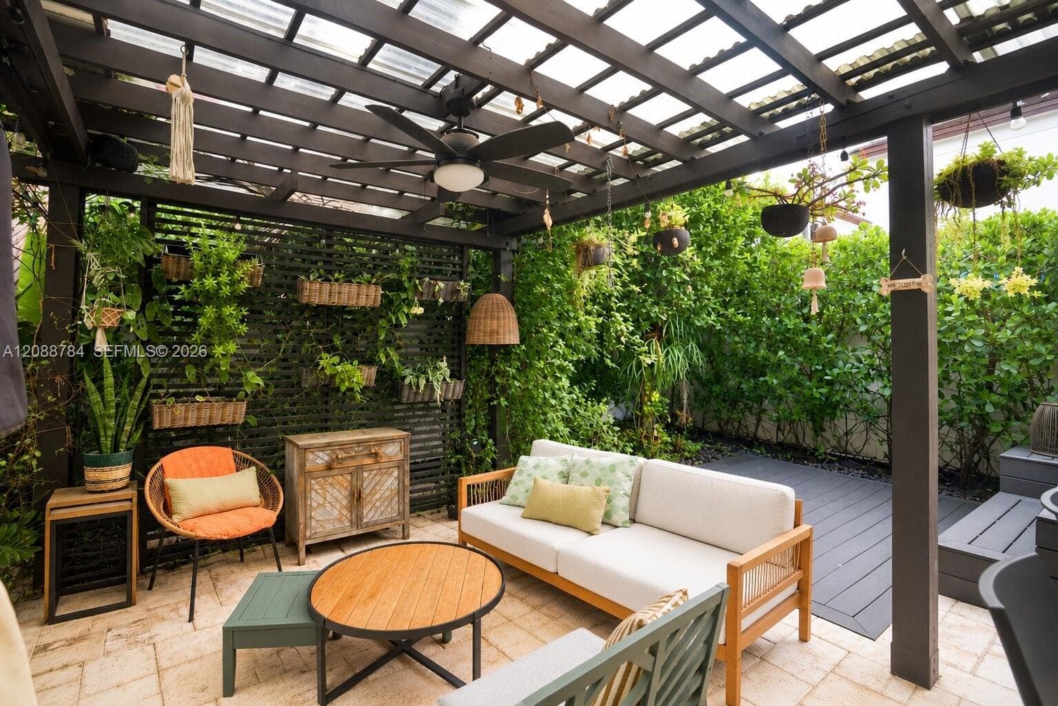 Outdoor patio featuring a dark wood pergola with a ceiling fan, a slatted privacy wall with integrated planters, and a paved stone surface
