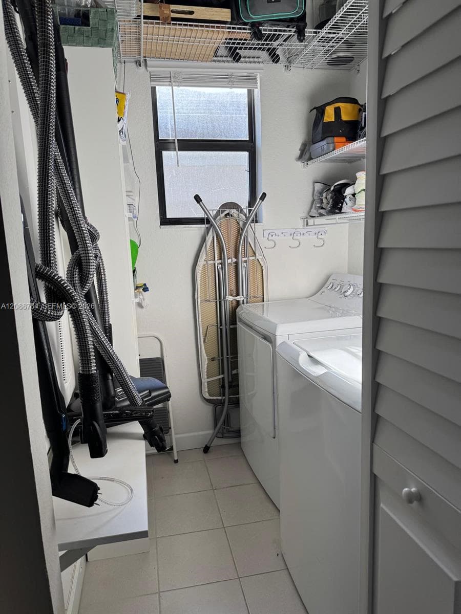 Laundry area featuring neutral tile flooring, built-in wire shelving, louvered closet doors, and a window providing natural light