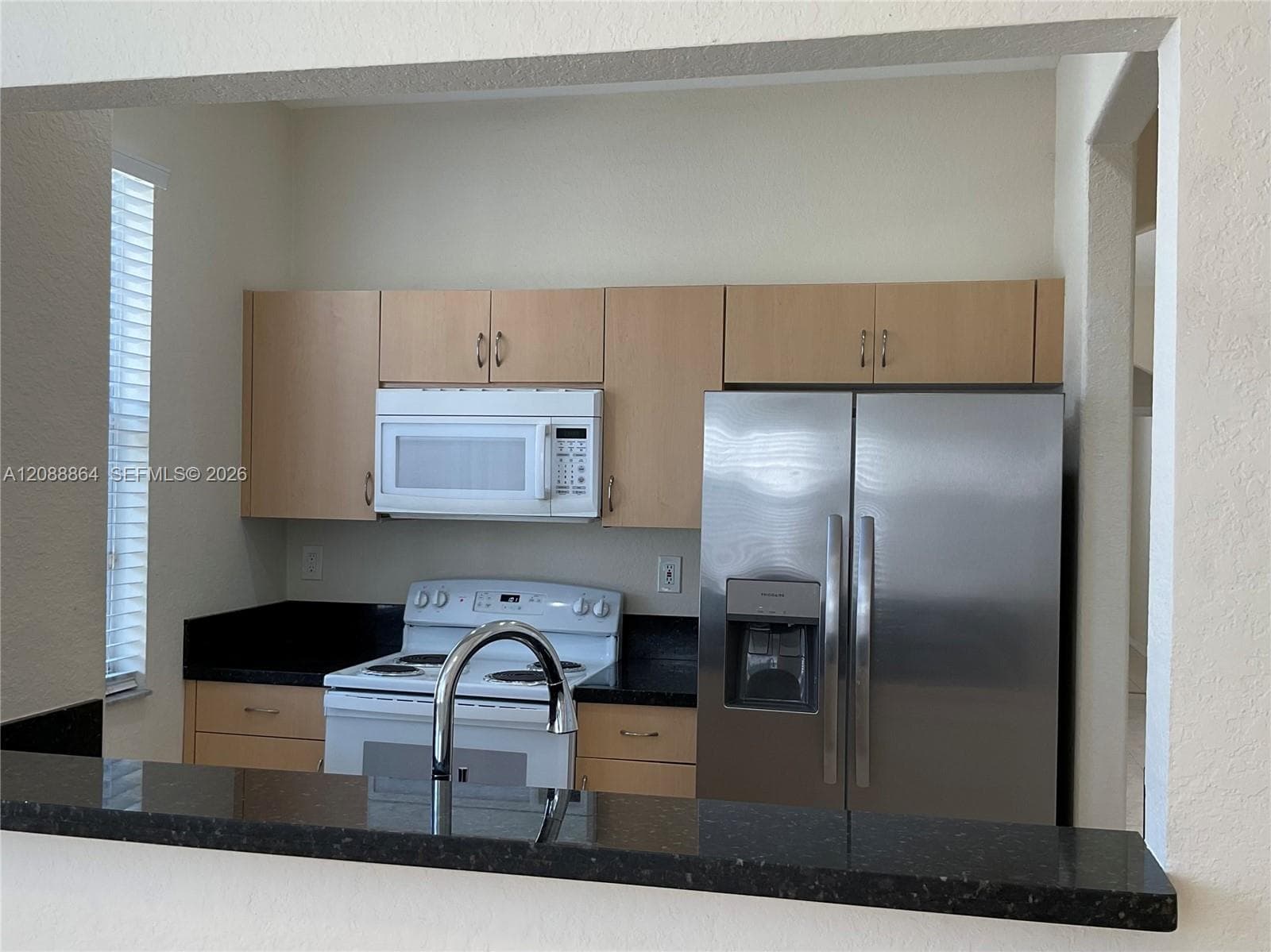 Kitchen featuring light-finish cabinetry, dark solid-surface countertops, a stainless steel refrigerator, white over-the-range microwave, and a white electric range
