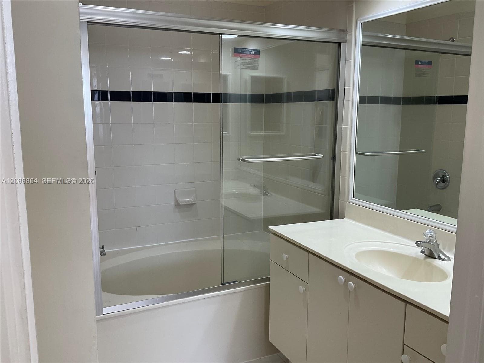 Bathroom featuring a vanity with an integrated basin, a large wall-mounted mirror, a tub-shower combination with a sliding glass door, and tiled wall surround with accent detail