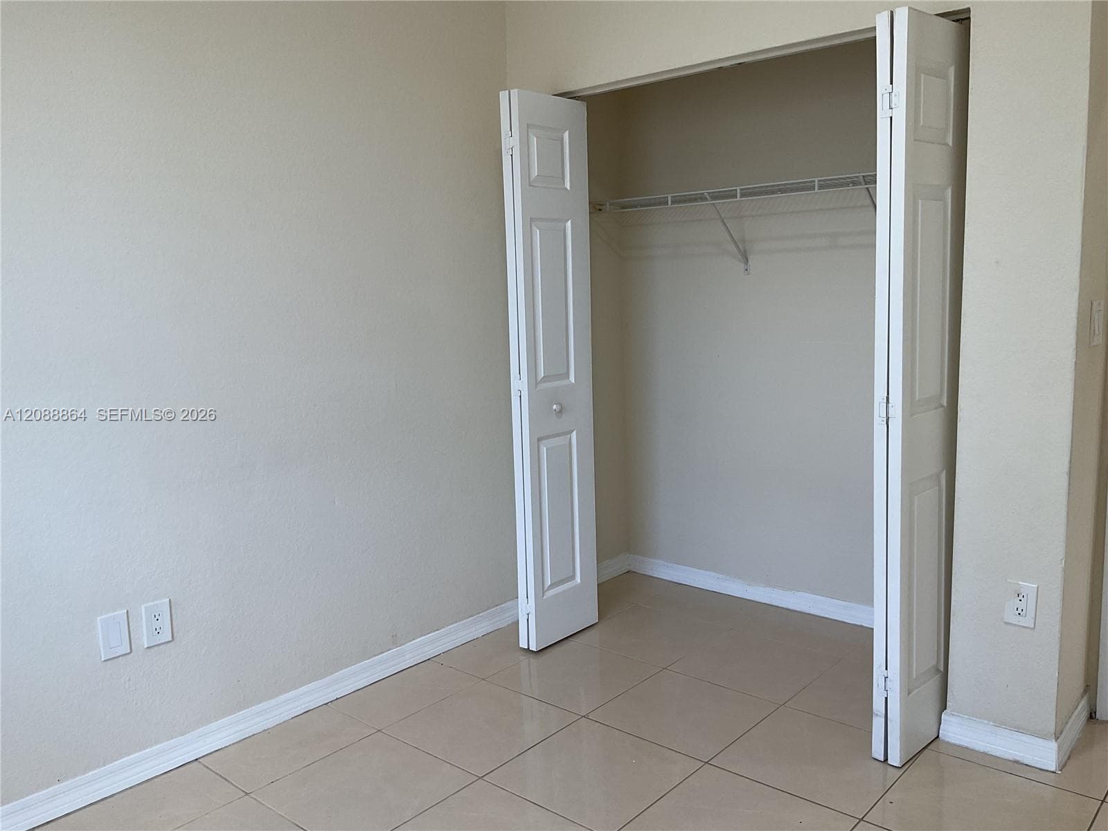 Neutral-toned interior space featuring light-colored tile flooring, bi-fold closet doors, and wire shelving