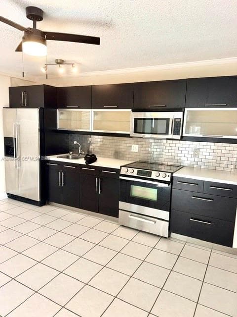 Kitchen featuring dark cabinetry with glass-front uppers, stainless steel appliances, subway tile backsplash, solid surface countertops, and white tile flooring