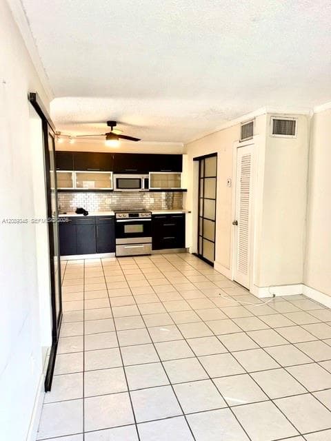Kitchen featuring dark cabinetry, stainless steel appliances, tiled backsplash, tile flooring, and sliding glass panel doors