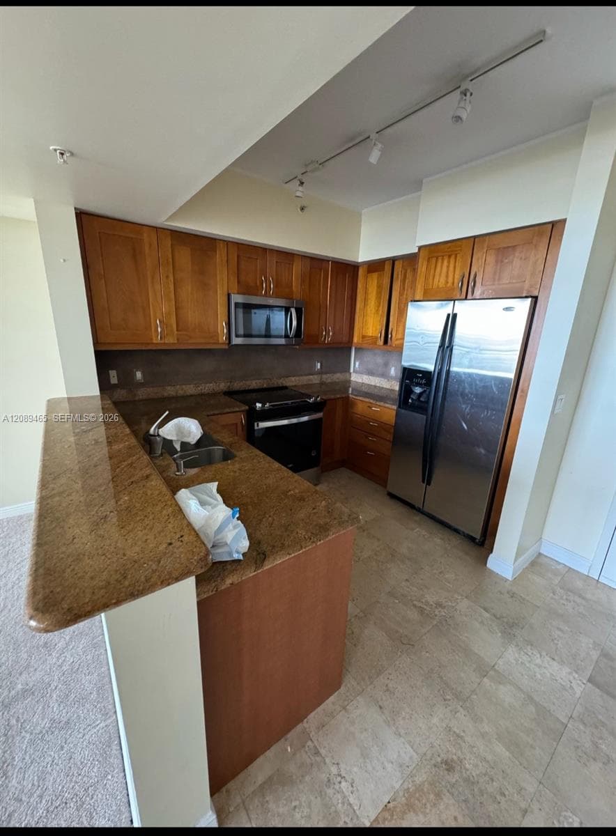 Kitchen featuring wood cabinetry, stone countertops, stainless steel appliances, tile flooring, and track lighting