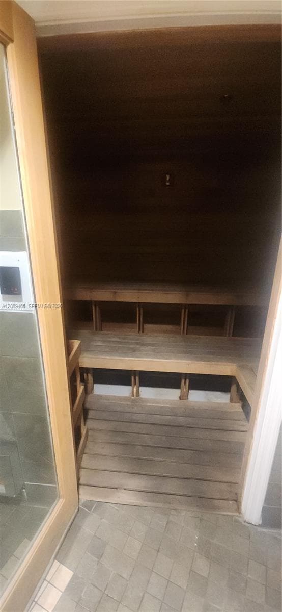 Sauna featuring wood-plank wall paneling, tiered wood bench seating, and a glass-paneled door