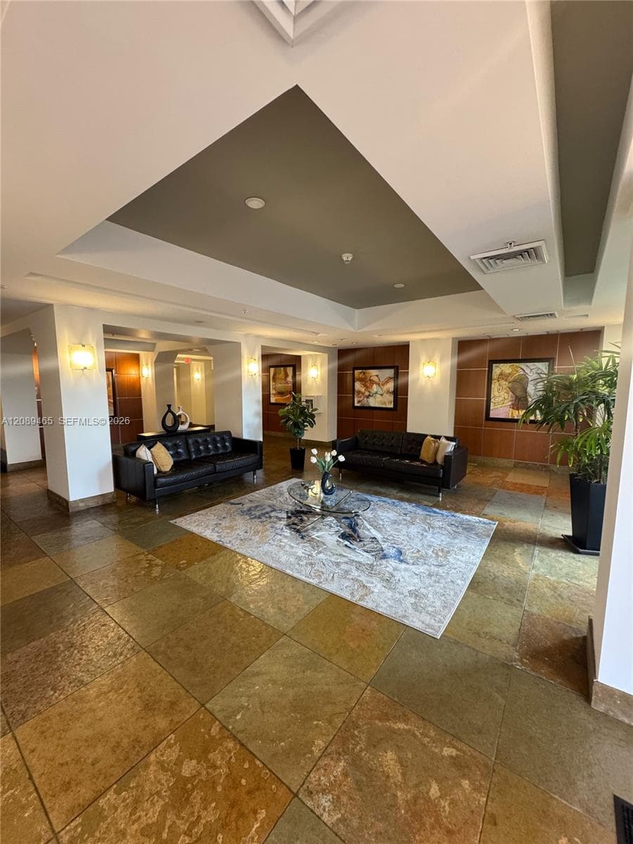 Large-format stone tile flooring, multi-tiered tray ceiling with recessed lighting, and wall-mounted sconces