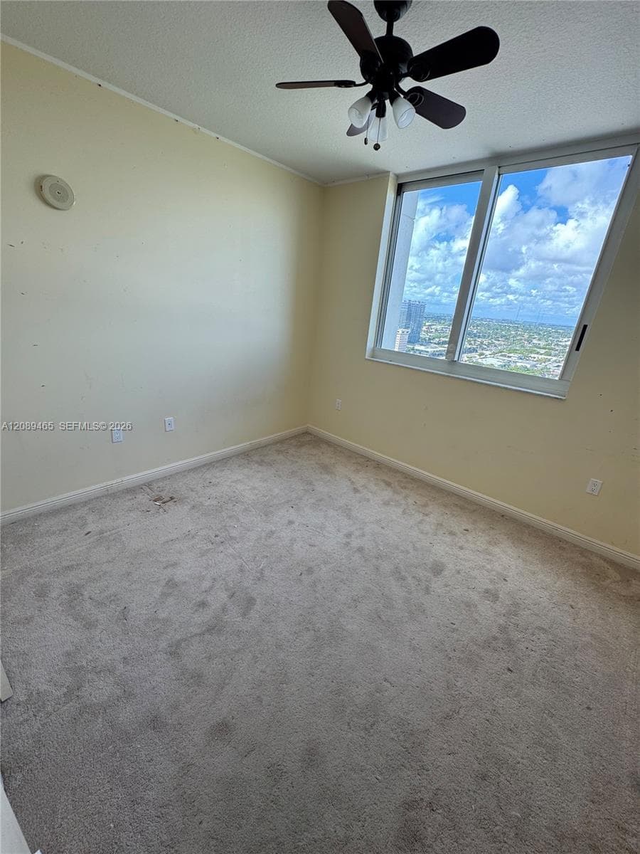 2nd bedroom again Room featuring large-scale windows with exterior cityscape, carpeted flooring, and a ceiling-mounted light fixture with integrated fan