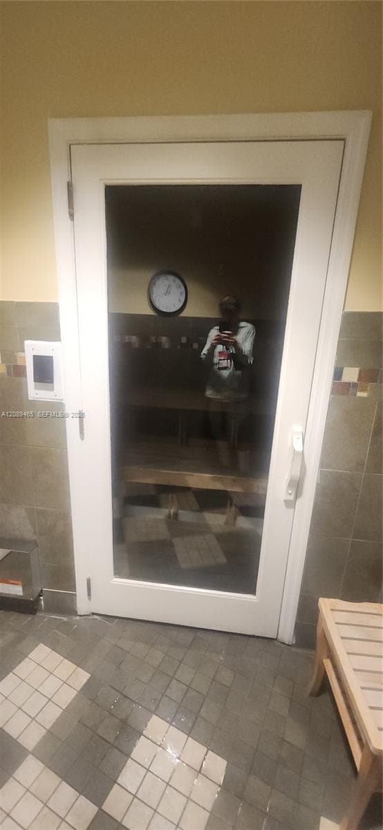 steam room featuring a white-framed glass door, interior wooden bench, and ceramic tile surround with multi-colored accent detailing