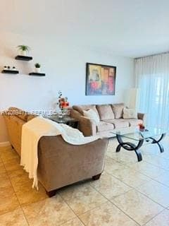 Living area featuring large-format neutral tile flooring, three tiered wall-mounted floating shelves, and full-length window coverings