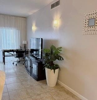 Neutral-toned interior space featuring large-format tile flooring, dual wall-mounted light fixtures, and a glass-paneled sliding door with full-length drapery