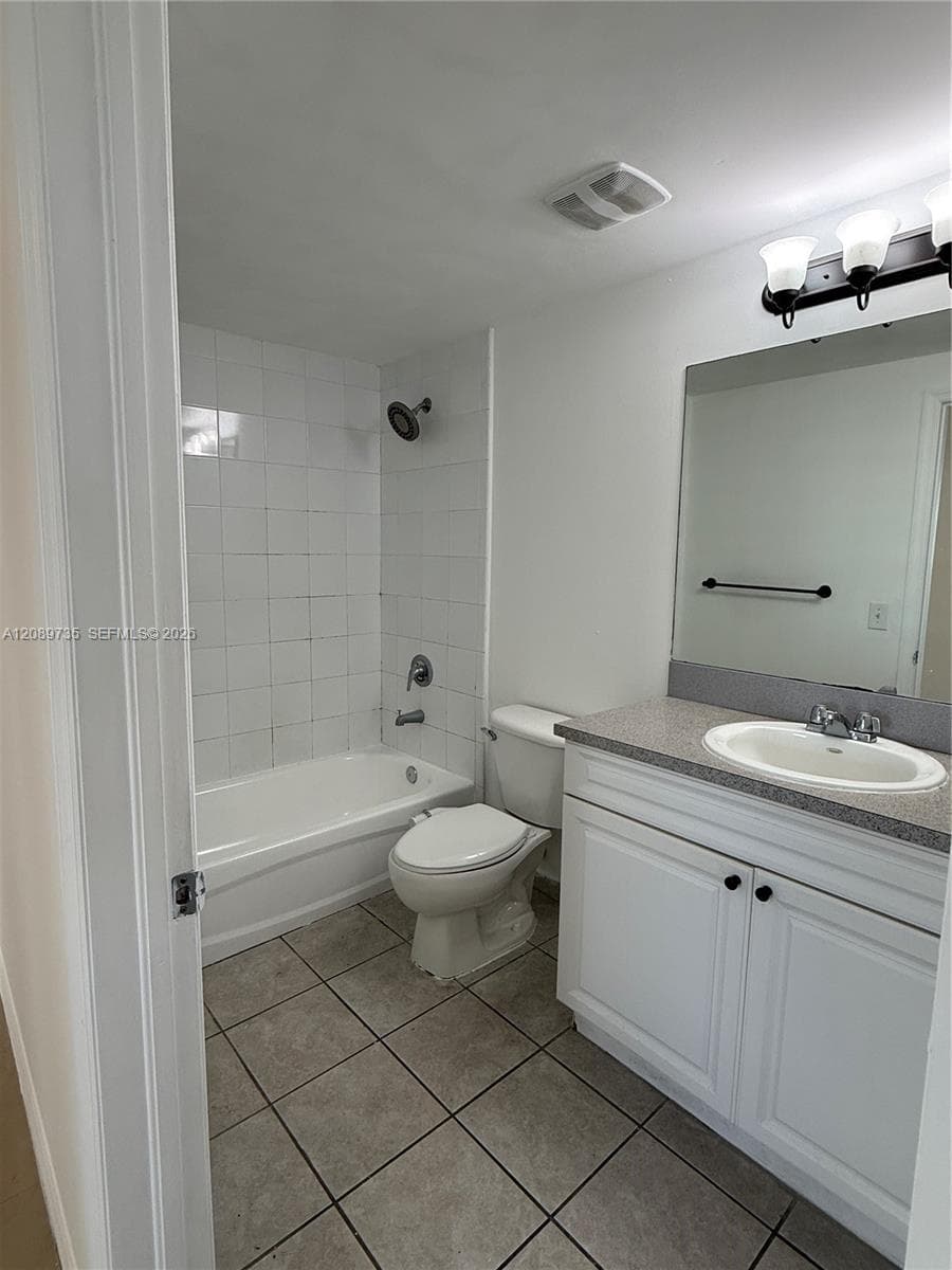 Bathroom featuring a white vanity cabinet with stone-finish countertop, white ceramic tile shower surround, tiled flooring, and a large wall-mounted mirror
