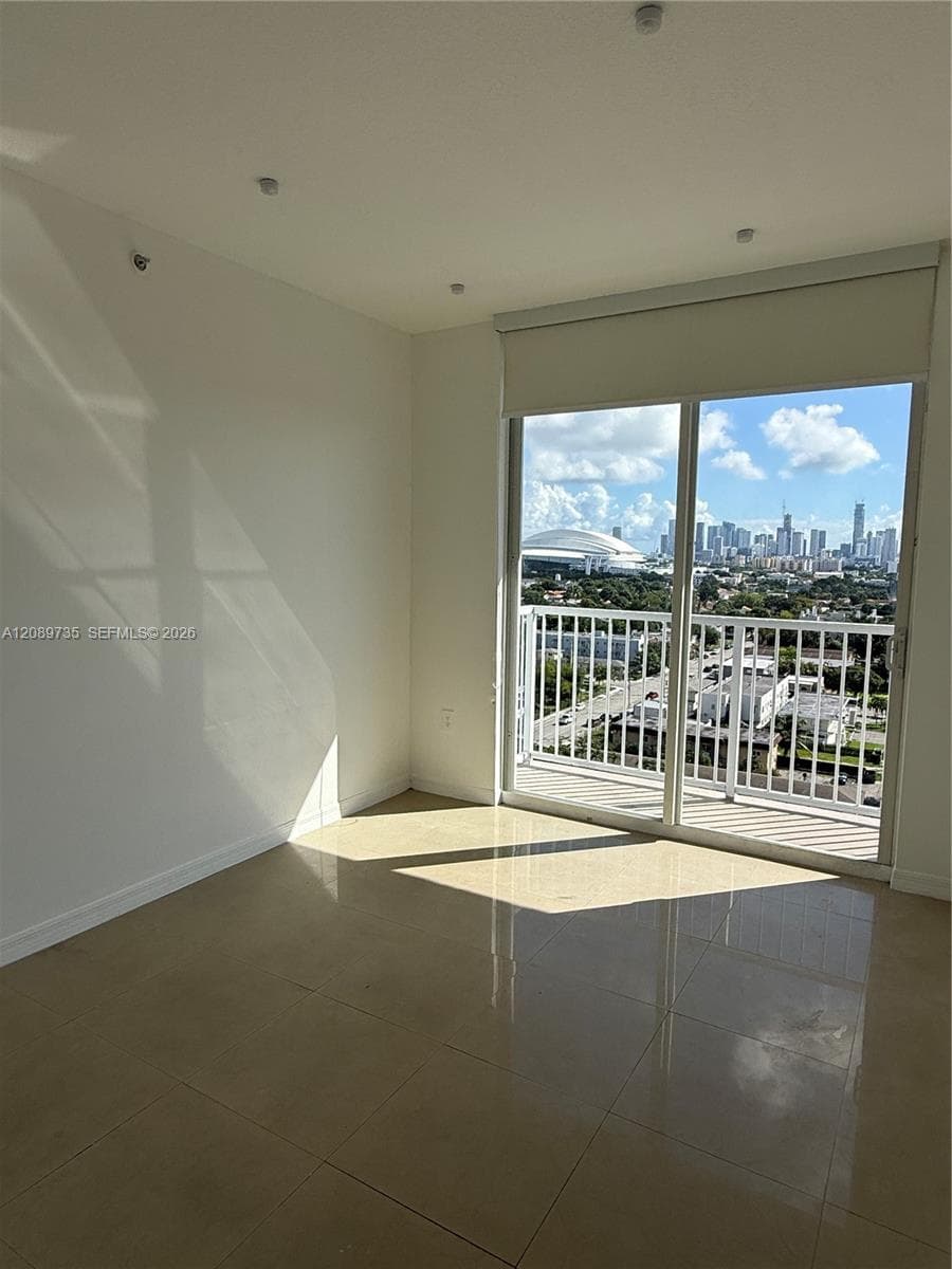 Polished tile flooring, recessed lighting, and expansive floor-to-ceiling glass sliding doors opening to a private balcony with an urban skyline backdrop