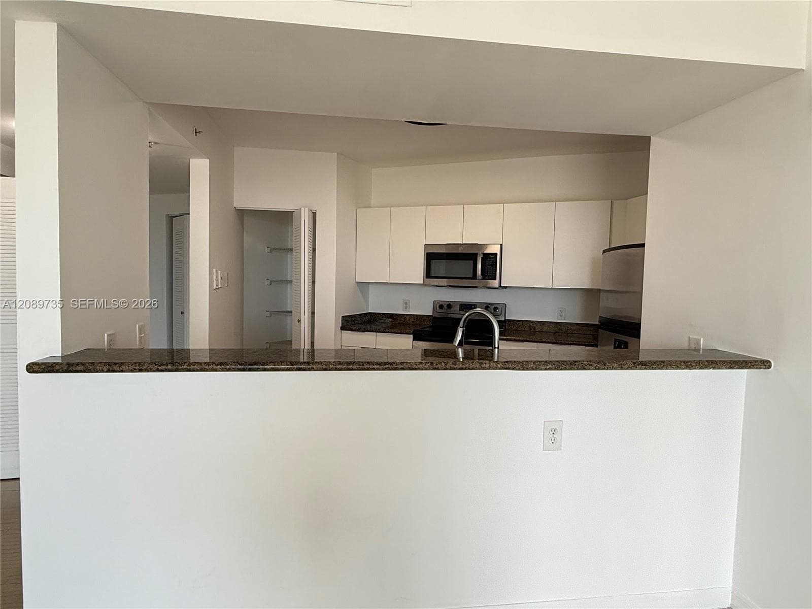 Kitchen featuring white flat-panel cabinetry, stone countertops, stainless steel appliances, and a built-in pantry