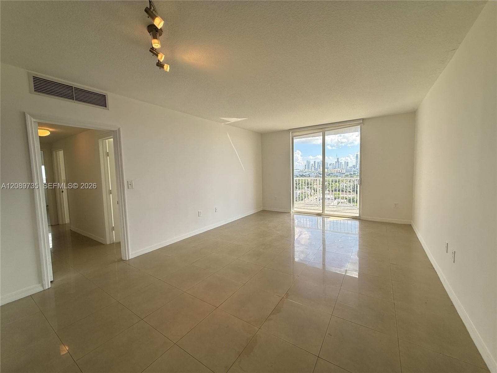 Open-concept interior featuring large-format tile flooring, multi-directional track lighting, and a sliding glass door providing access to an exterior balcony