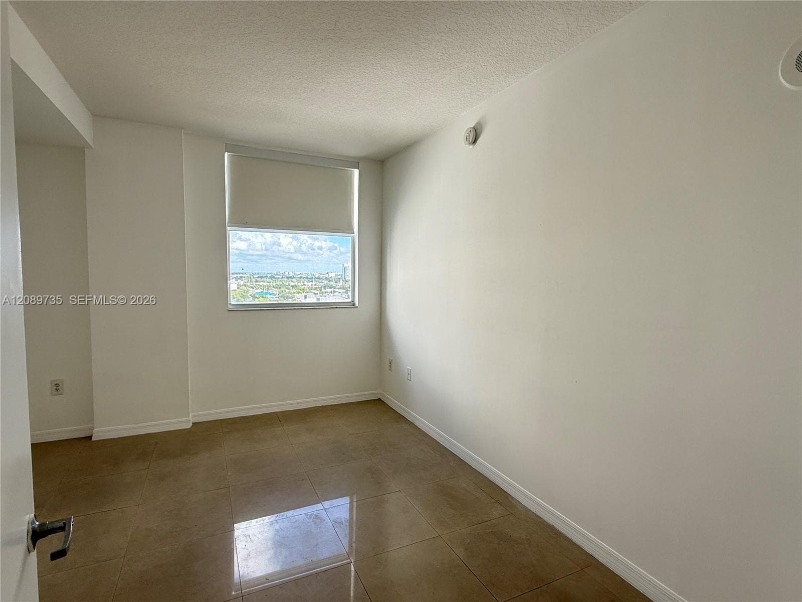 Interior room featuring large-format tile flooring, neutral walls, and a single window with a solar shade