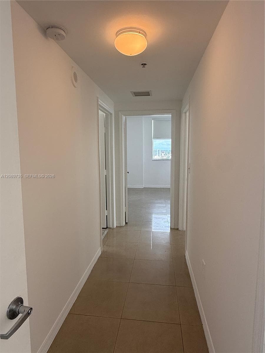 Hallway featuring neutral-toned tile flooring, minimalist door frames, and a flush-mount ceiling light fixture