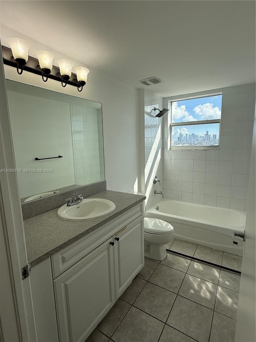 Bathroom featuring white cabinetry, solid surface countertop with an integrated sink, four-light vanity fixture, and a tile-surround tub