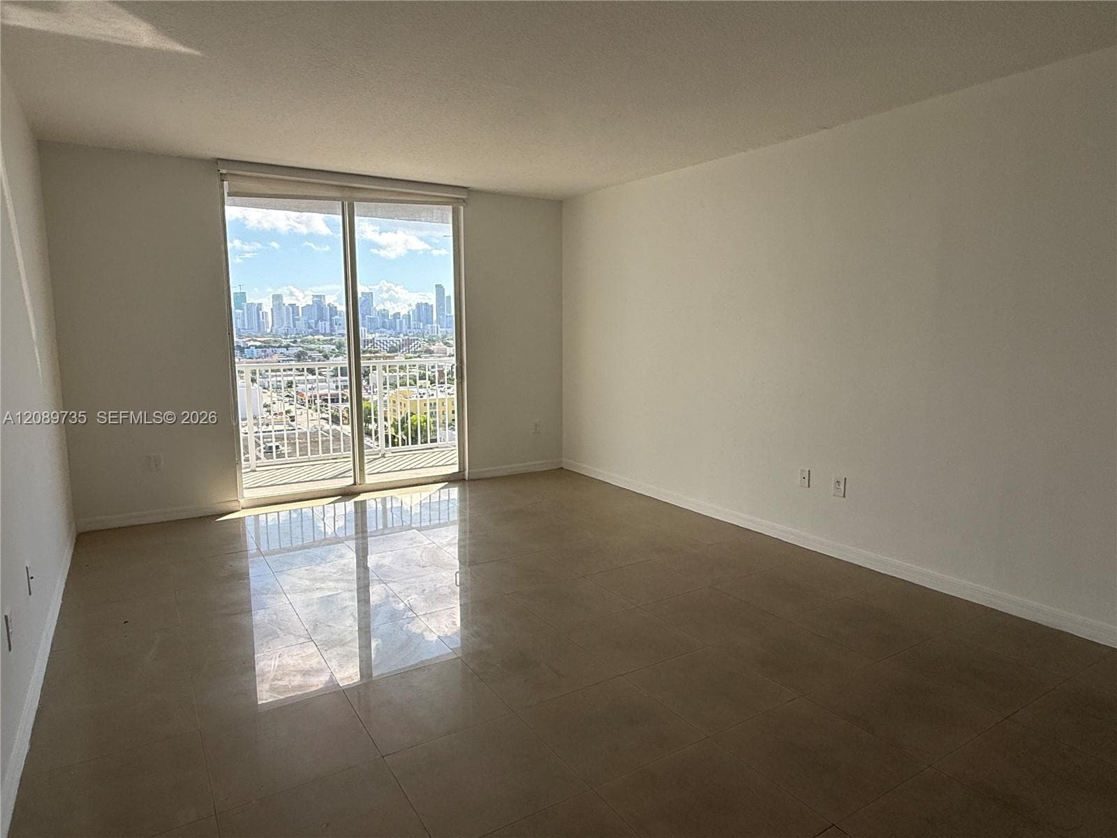 Open-concept room featuring large-format tile flooring, a sliding glass door, and a balcony with cityscape scenery