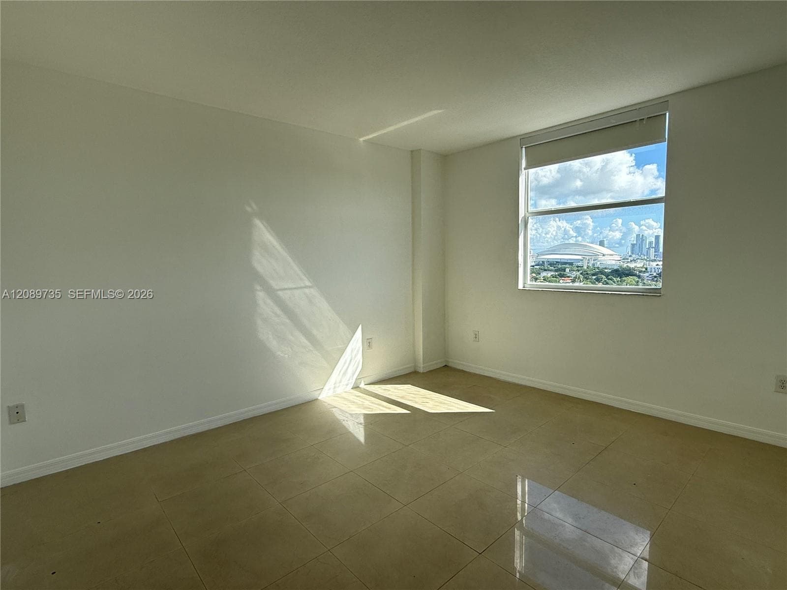 Neutral-toned tile flooring, minimalist white walls, and a large window featuring an urban skyline backdrop