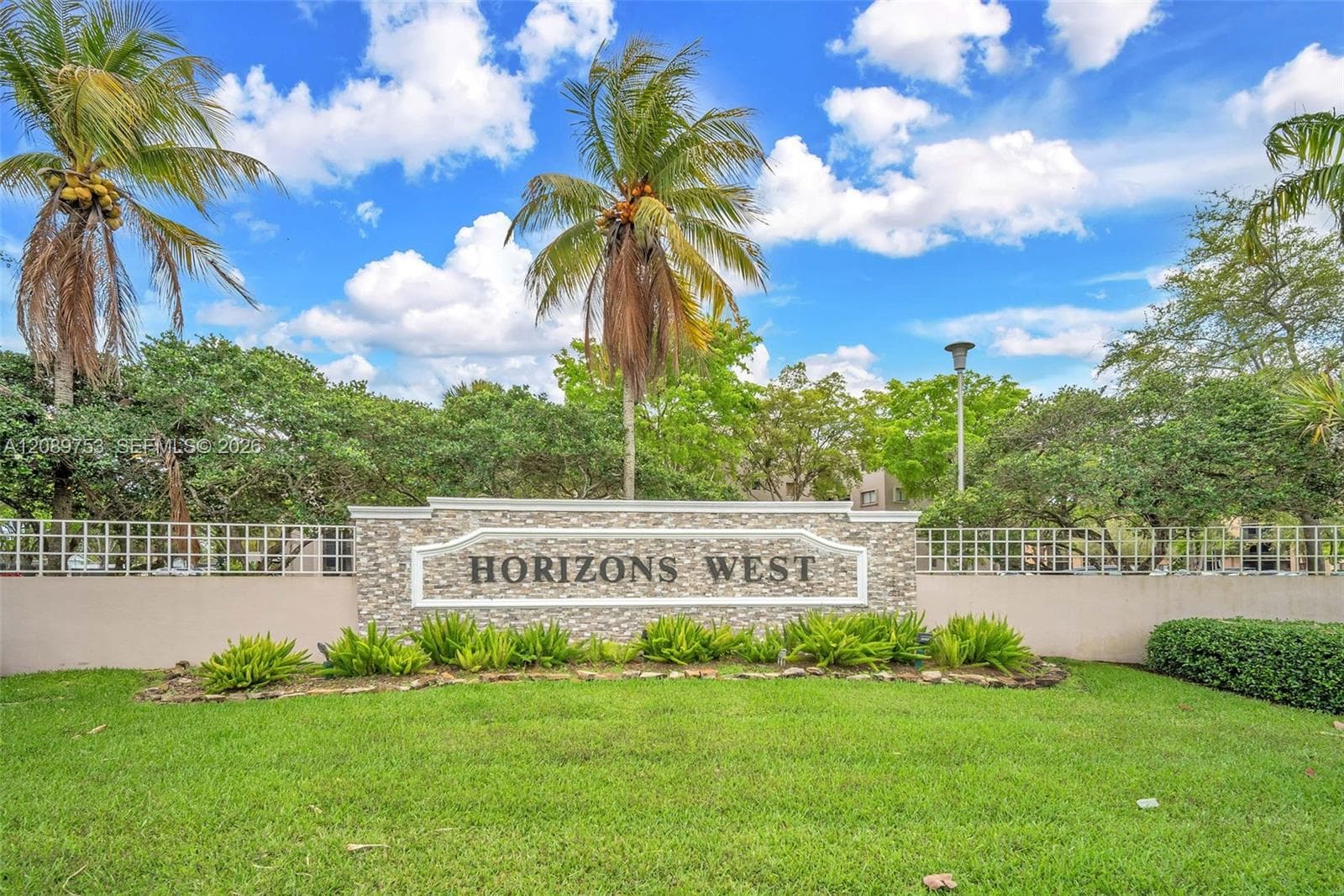 Stone-accented community monument sign featuring integrated landscaping with mature palm trees and manicured lawn