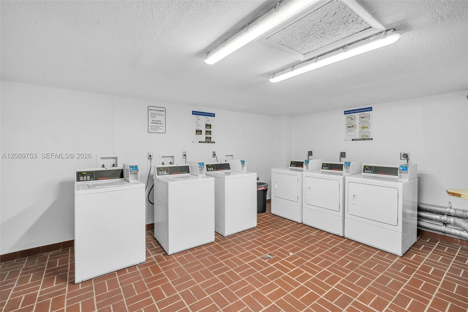 Laundry facility featuring multi-unit washing machines and dryers, ceramic tile flooring, and dual overhead light fixtures