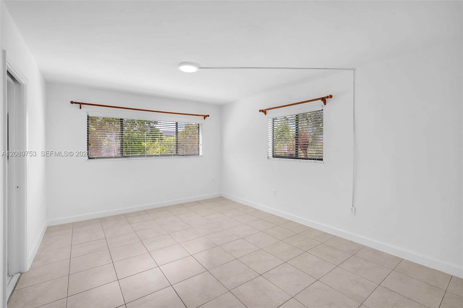 Neutral-toned tile flooring, dual windows with horizontal blinds, and a flush-mount overhead light fixture