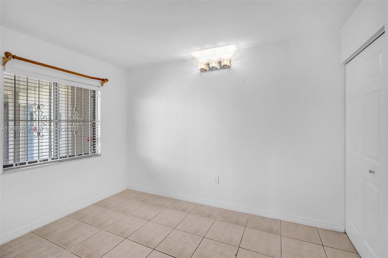 Ceramic tile flooring, multi-panel closet door, window with decorative security bars, and wall-mounted multi-bulb light fixture