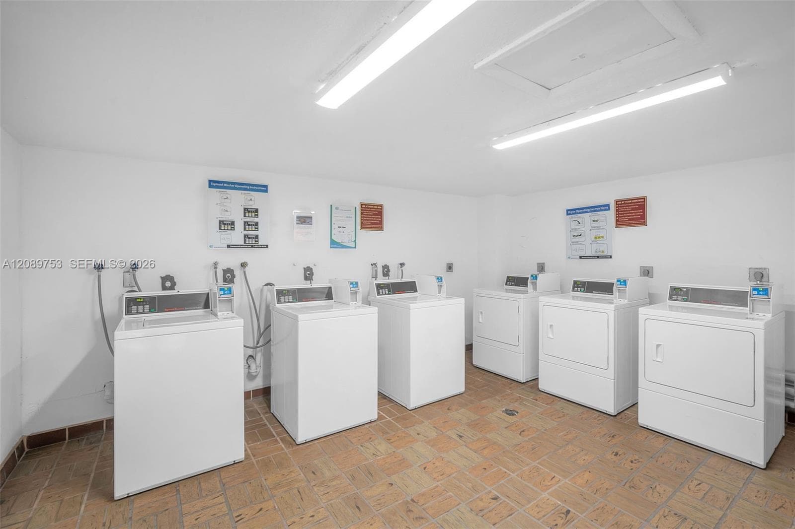 Laundry facility featuring multiple washer and dryer units, tile flooring, and overhead fluorescent lighting