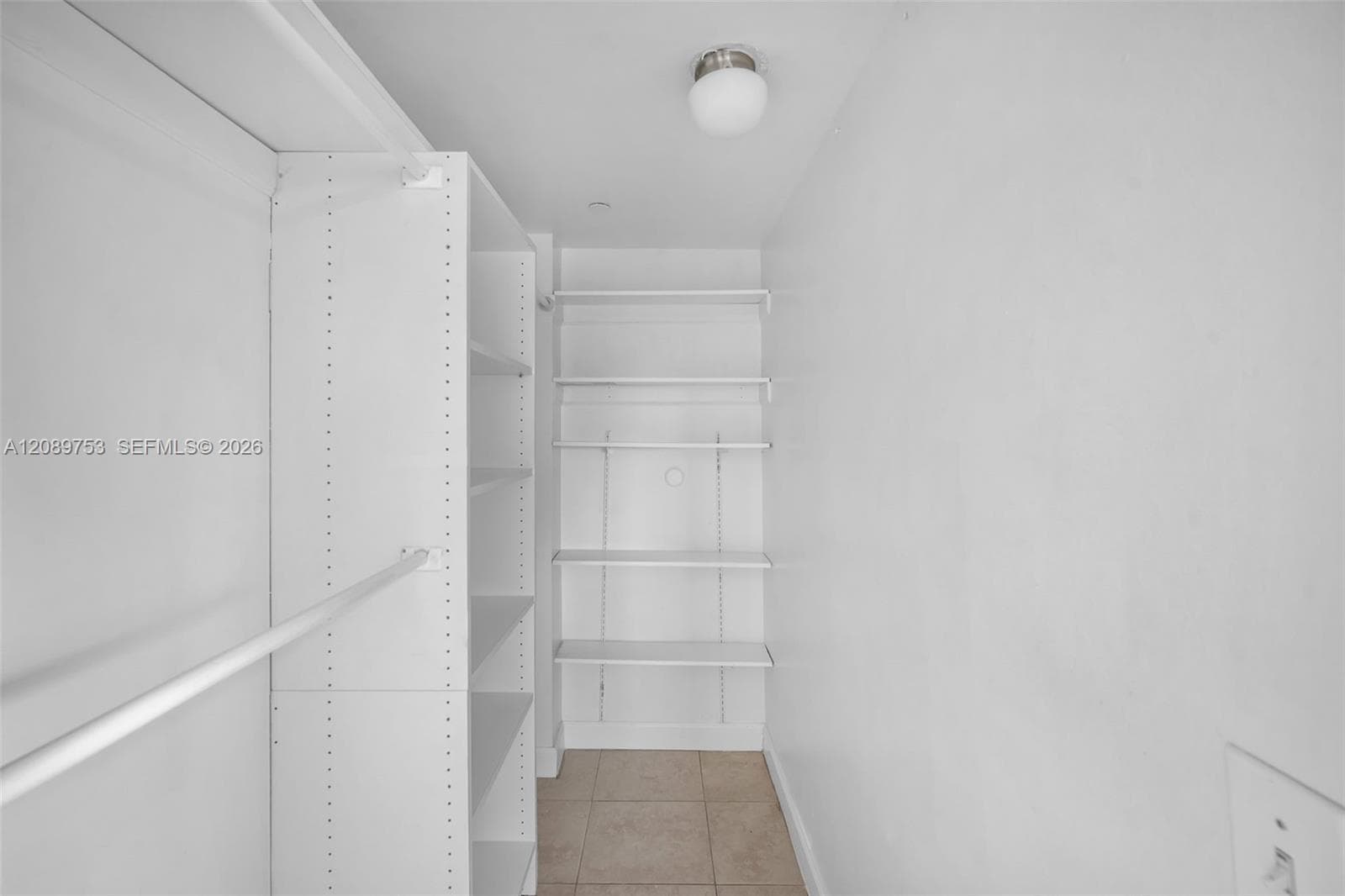 Storage area featuring adjustable white shelving units, a hanging rod, ceiling-mounted globe light fixture, and tile flooring