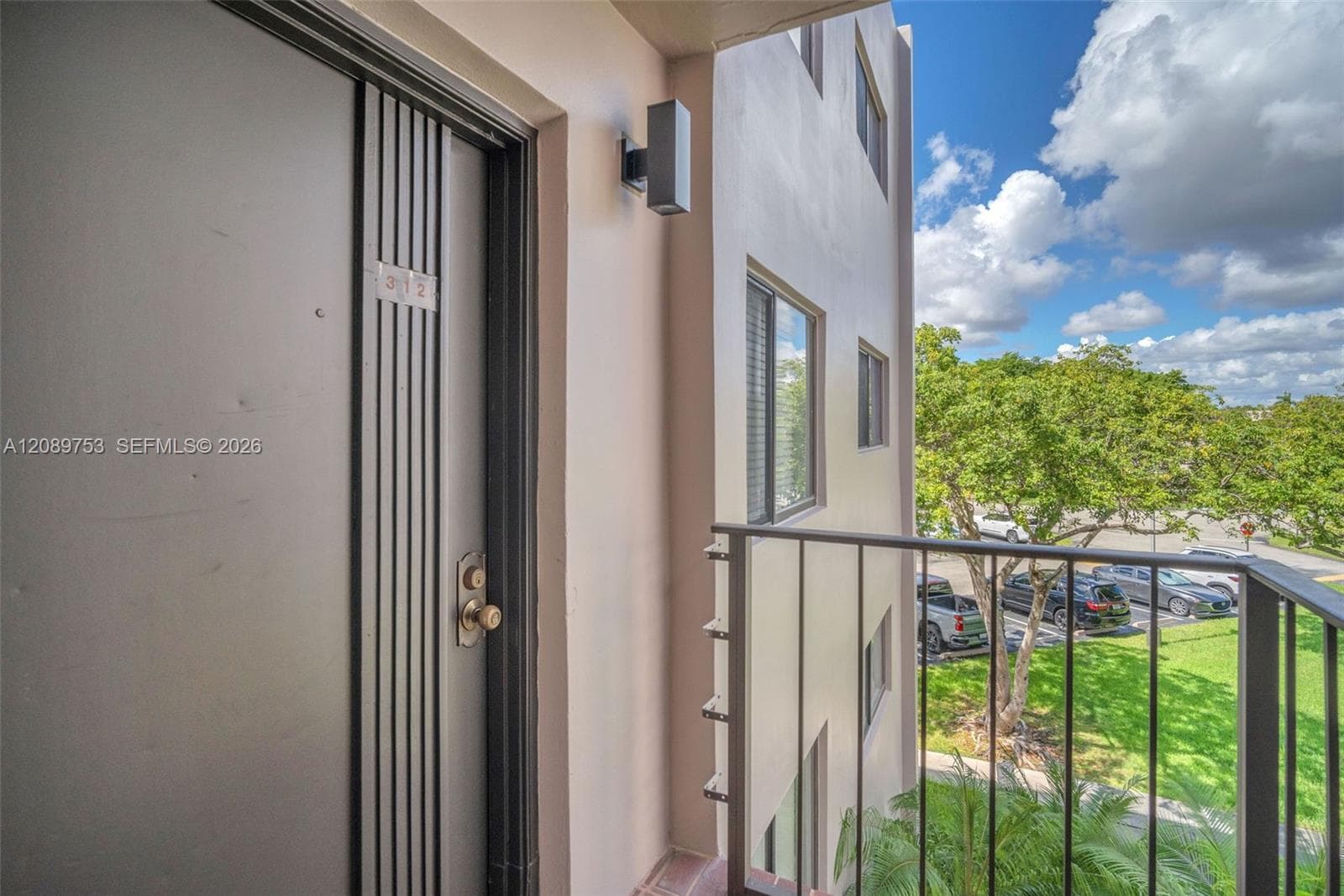 Exterior balcony with metal railings, flush-mount wall-mounted exterior light fixture, and vertical paneling entry door