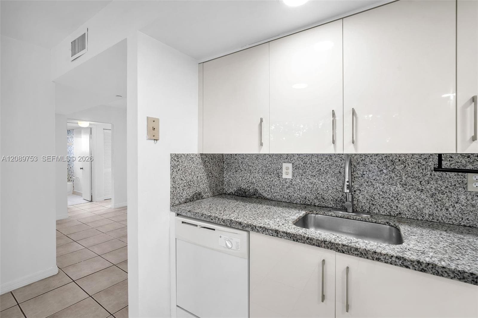 Kitchen area featuring high-gloss white cabinetry, stone-finish countertops, undermount stainless steel sink, pull-down faucet, and built-in dishwasher
