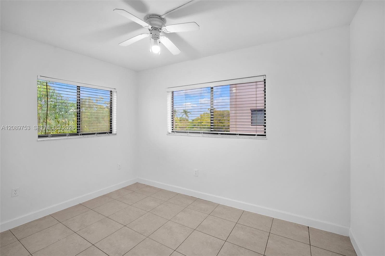 Neutral-toned tile flooring, dual windows with horizontal blinds, and a central ceiling fan with an integrated light fixture