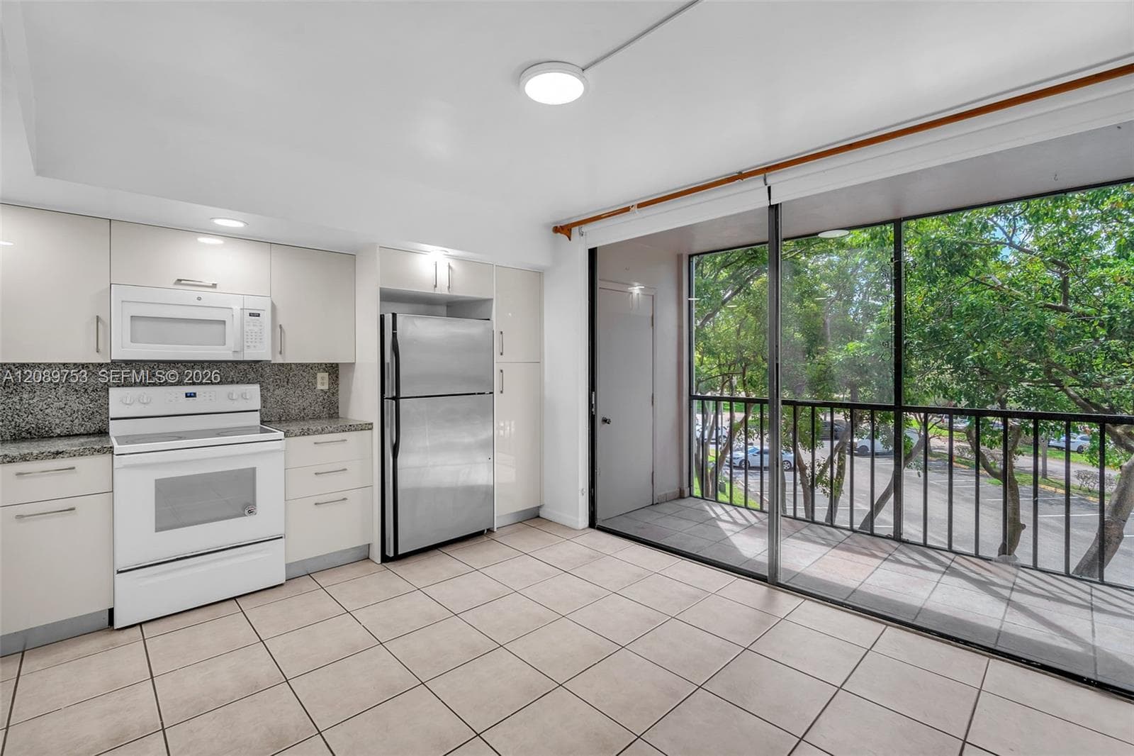 Kitchen featuring flat-panel cabinetry, stone-finish countertops, stainless steel refrigerator, white range with overhead microwave, and ceramic tile flooring, with access to a railed balcony