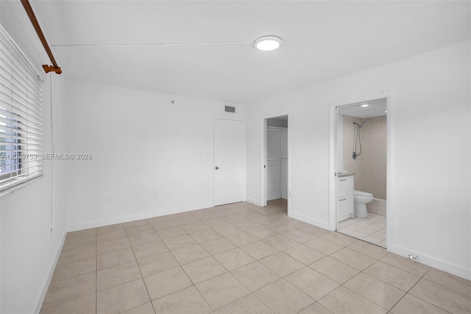 Neutral-toned tile flooring, horizontal slat window blinds, and solid core interior doors