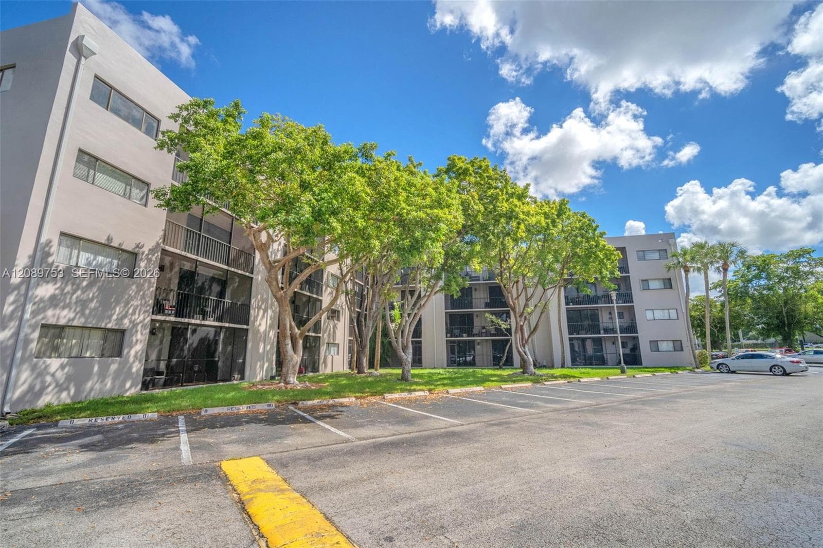Multi-story exterior featuring smooth stucco facade, screened balconies, and asphalt-paved parking