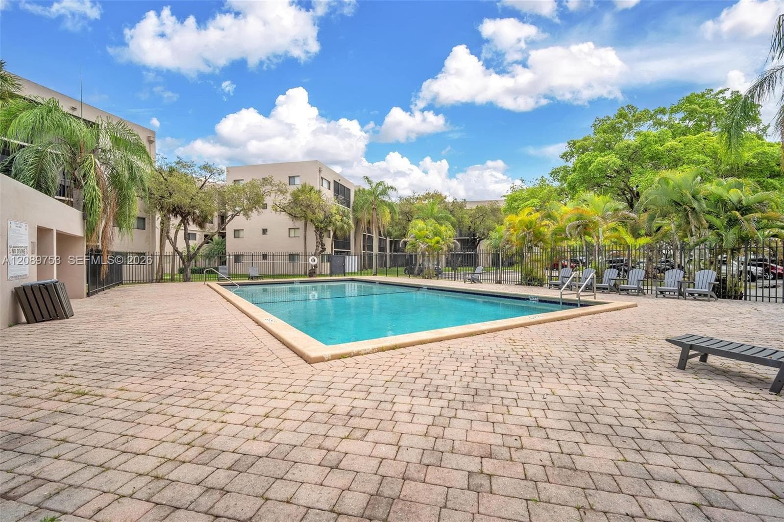 Rectangular swimming pool featuring a light-toned brick paver deck and metal perimeter fencing