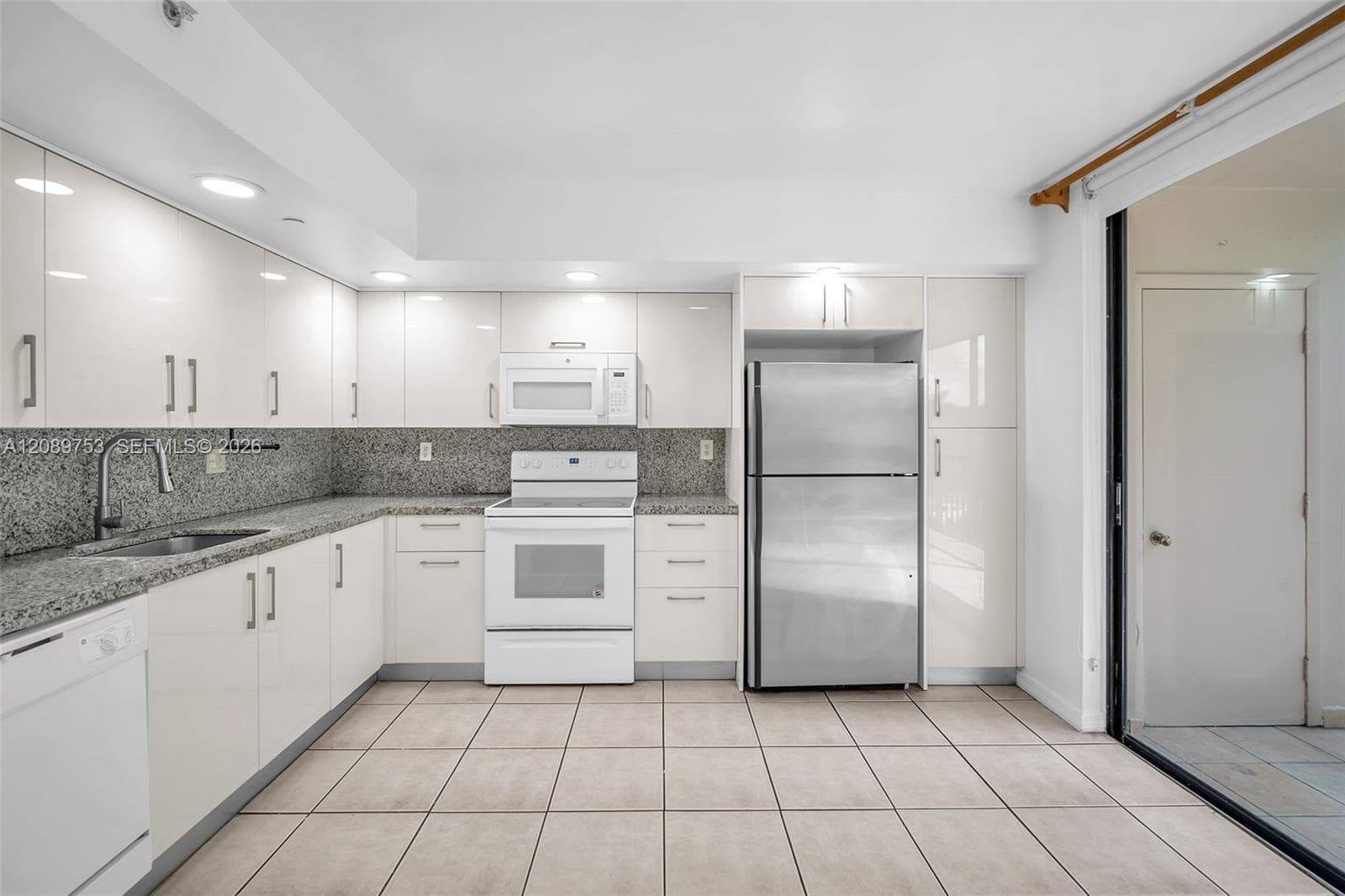 Kitchen featuring high-gloss white cabinetry, stone countertops, integrated stainless steel appliances, recessed lighting, and tile flooring