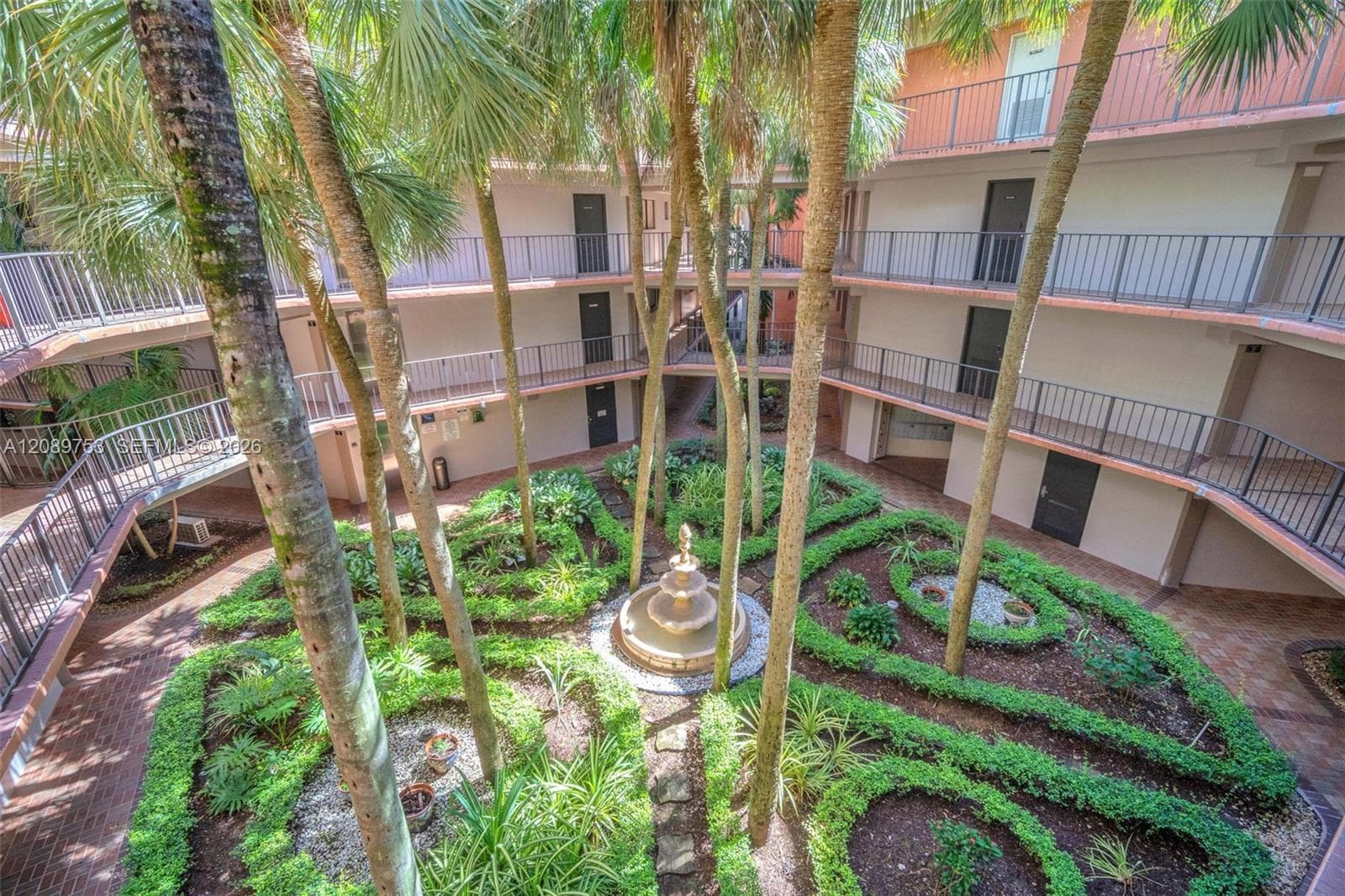 Courtyard featuring tiered landscaping, a central stone fountain, mature palm trees, and multi-level walkways with metal railings