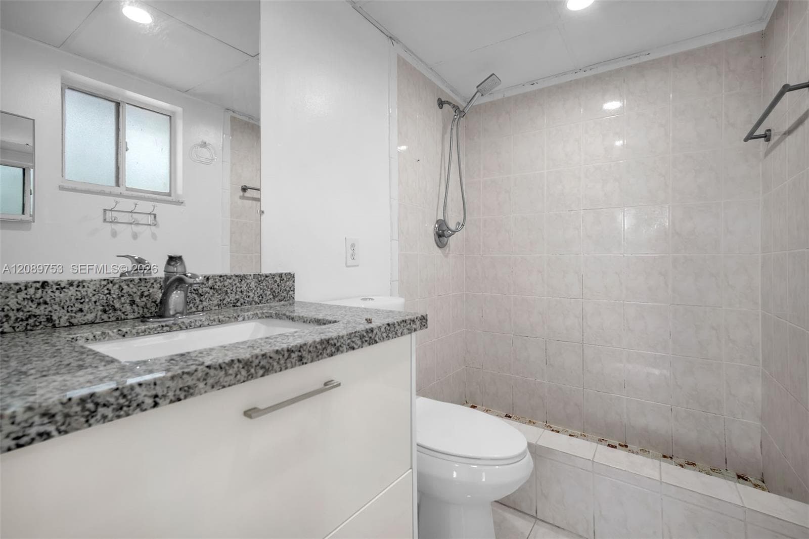 Bathroom featuring a white vanity with stone-finish countertop and integrated sink, chrome faucet hardware, and a tiled shower enclosure with a handheld showerhead