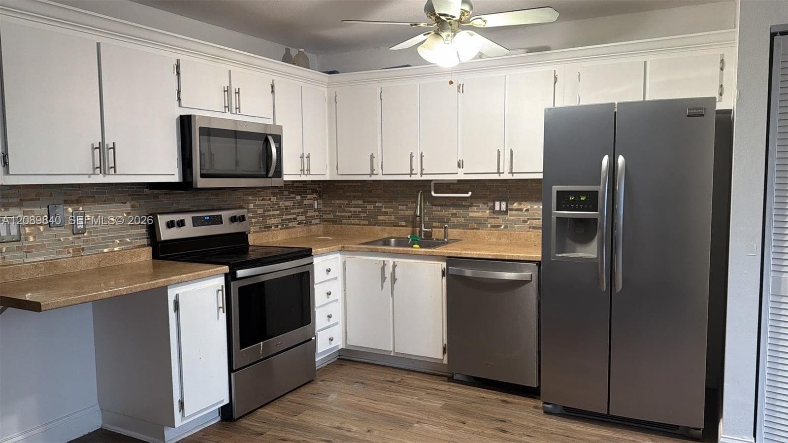 Kitchen featuring white cabinetry, stainless steel appliances, multi-toned tile backsplash, solid-surface countertops, and wood-finish flooring