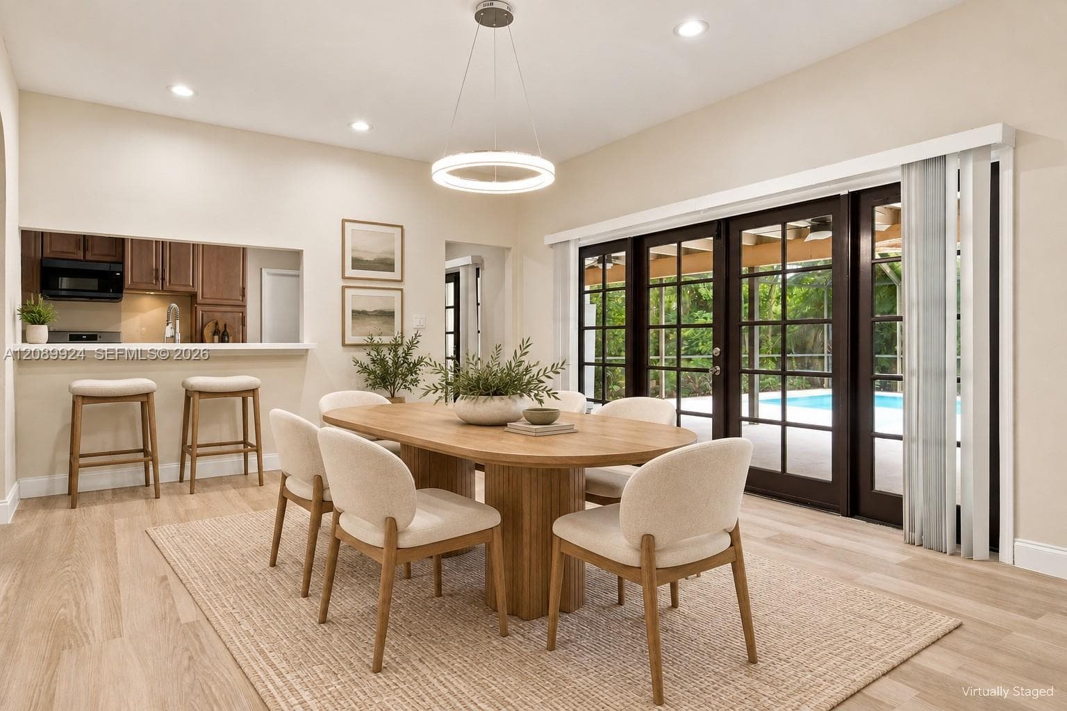 Wood-finish flooring, recessed lighting, modern circular pendant fixture, pass-through opening to kitchen, and multi-panel glass doors